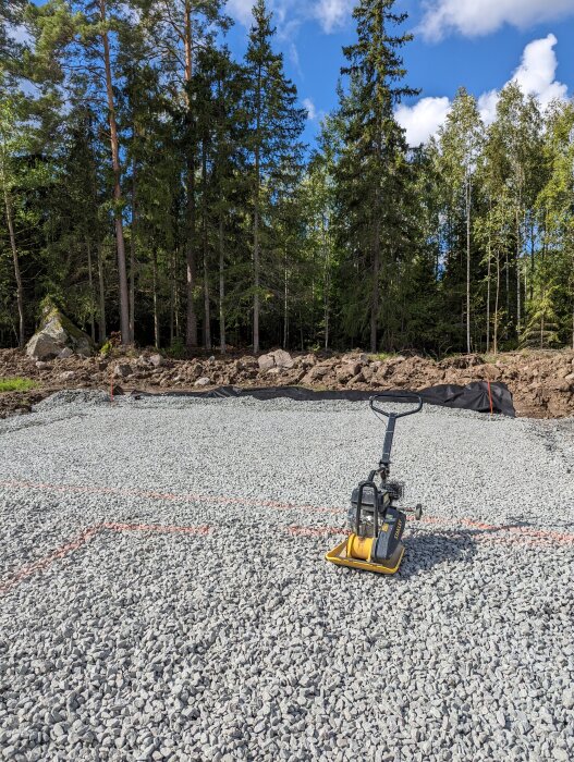 Byggarbetsplats, grus, skogsbakgrund, packningsmaskin, klar himmel, stenar, markarbeten, ute i naturen.