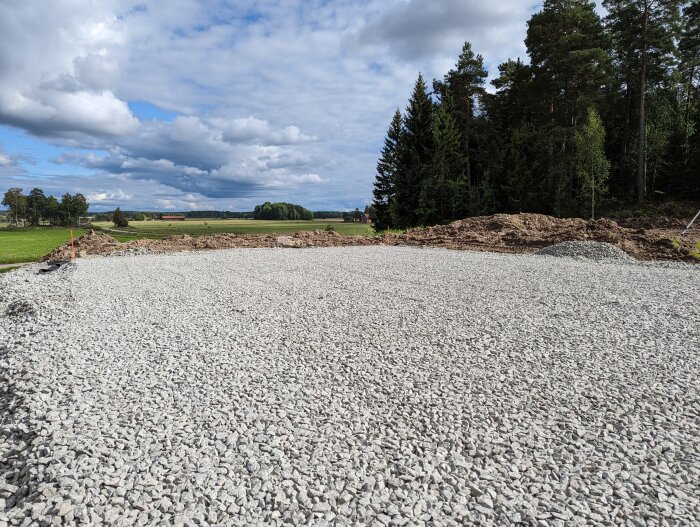 Grusplan, jordhögar, skog, delvis molnig himmel, potentiell byggarbetsplats på landsbygden.