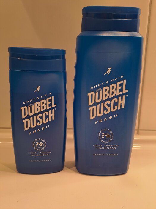 Två blå flaskor märkta "DUBBEL DUSCH FRESH" för kropp och hår.