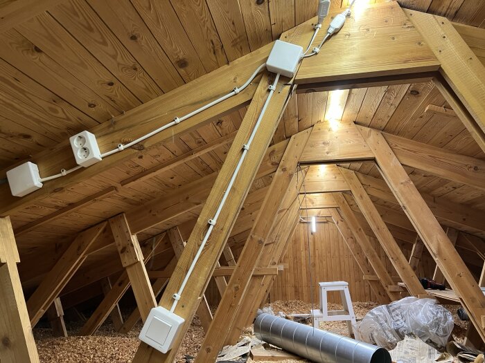 Träbjälkar i taket, isolering på golvet, ventilationstrumma, elinstallationer, oinredd vind eller loft.
