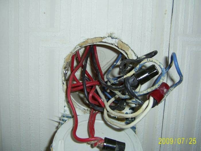 Oorganiserad elinstallation med exponerade kablar och ledningar inne i vägguttag. Potentiell fara. Behöver elektrikers uppmärksamhet.