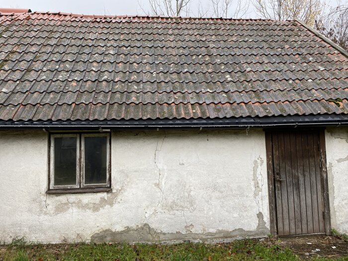 Gammalt hus med tegeltak, fönster, trädörr, sliten fasad.