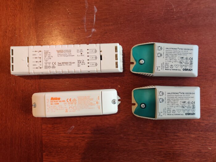 Fyra elektroniska transformatorer för halogenlampor på ett träbord. Märkena är Vossloh, Relco, och Osram.