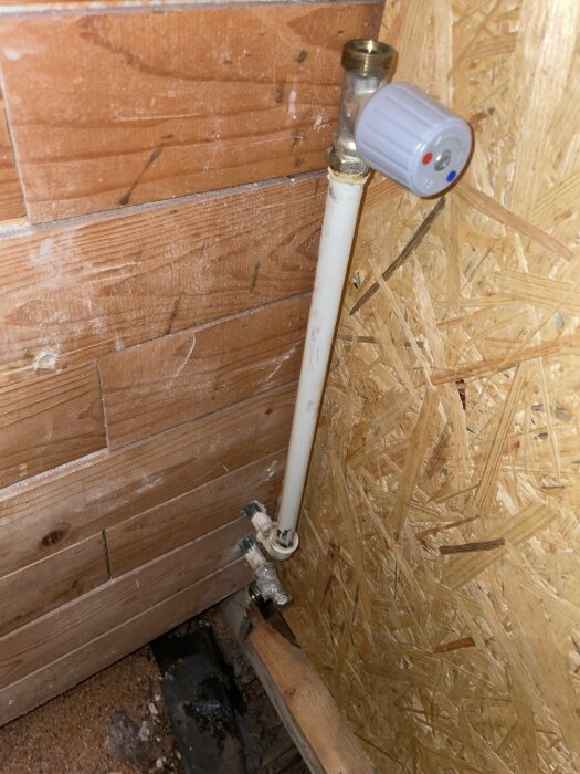 Ett vattenrör med en termostatventil i ett ofärdigt trärums hörn.