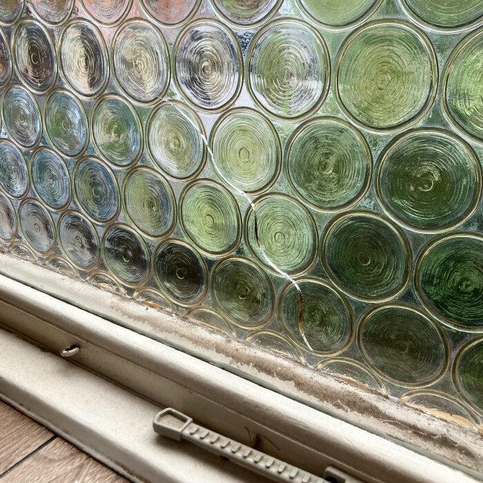 Glastegelvägg med cirkulära mönster, olinjerade kulörer, fönsterbräda och handtag i förgrunden.