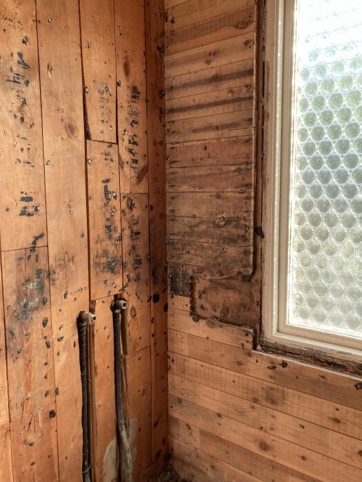 Trähörn i rum med rör och skador, bredvid fönster med bubbelglas.