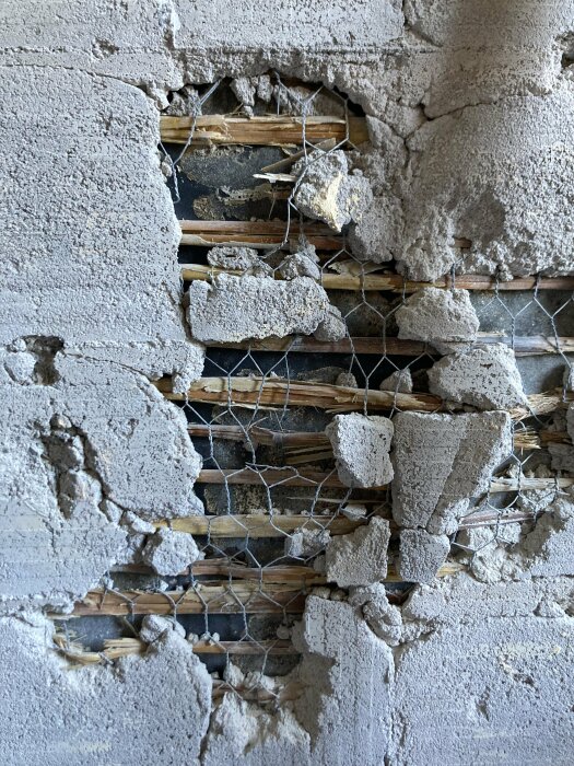 Ett hål i en murad vägg visar lager av murbruk, nät och träribbor. Slitage eller renoveringsarbete synligt.