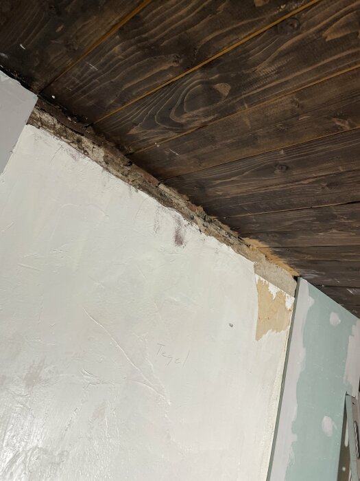 Renovering pågår, tak och vägg möts med spricka, mörkt trä, ordet "Tegel" skrivet på väggen.