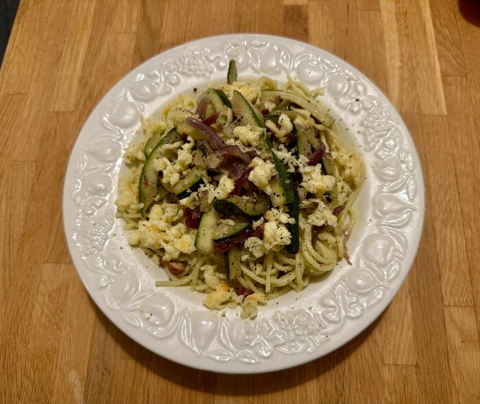 Pasta med fetaost, grönsaker, rödlök på vit tallrik, tillagad måltid, mångfärgad, hemmamiddag, träbordsbakgrund.