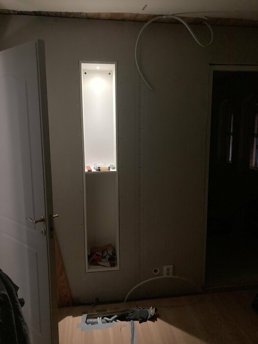 Ett rum under renovering med oskyddade kablar, gipsskivor och en oslipad dörr.