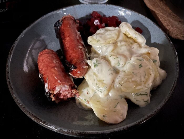 Mörk tallrik med korv, gräddsås-täckta potatisar och rödbetor.