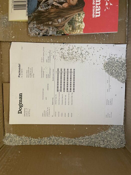 En packsedel på kartong, strössel av material, del av katalog synlig uppåt.