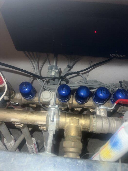 VVS-installation med rör, ventiler och styrenhet märkt "Uponor." Rörigt utseende, tekniskt rum eller skåp.