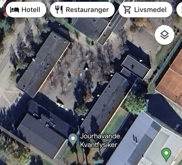 Satellitbild över byggnader med träd, markering för "Jourhavande Kvantfysiker", samt navigationsikoner för hotell, restauranger och livsmedel.