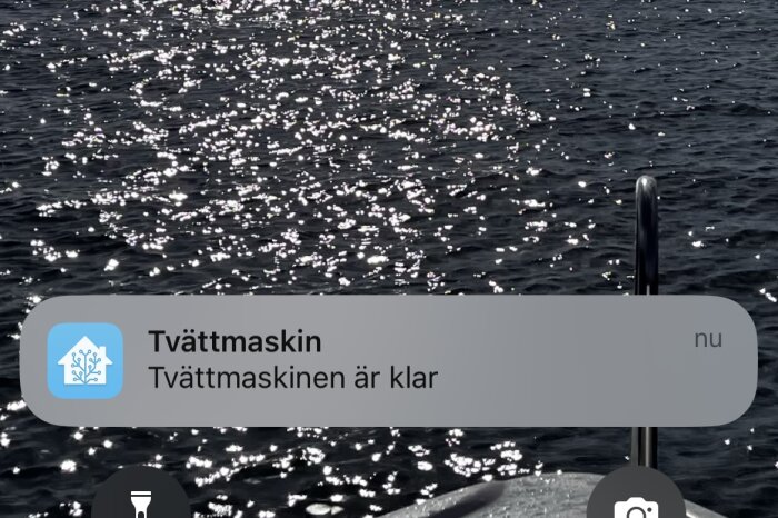 Solreflekterande vatten, mobilskärm, pop-up notis: "Tvättmaskinen är klar".