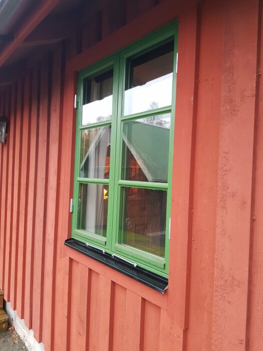 Röd stuga, grönt fönster, reflektion, traditionell svensk arkitektur, träpanel, utomhus.