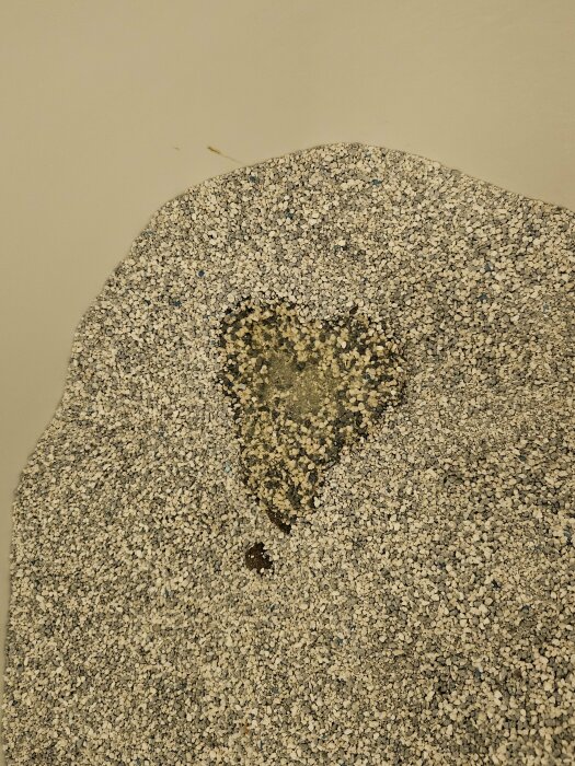 Texturerad yta med hjärtformad färgskillnad, småstenar, lite skräp, beige bakgrund, slitage eller fläck.