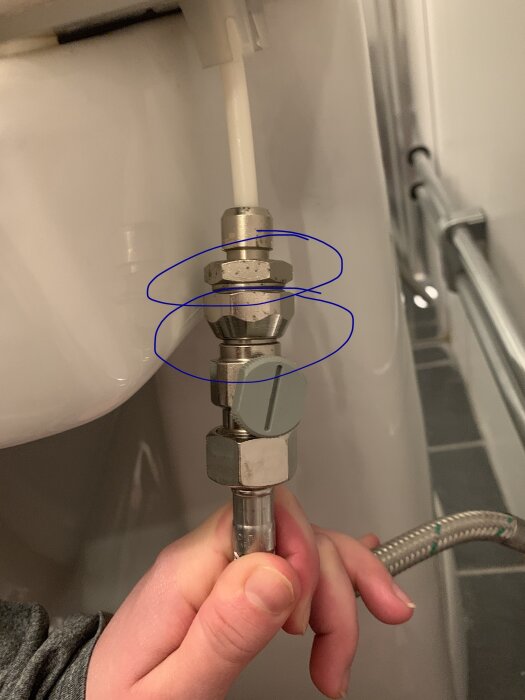 Hand kopplar loss vattenslang från toalettens botteninlopp för reparation eller underhåll med blå markering.