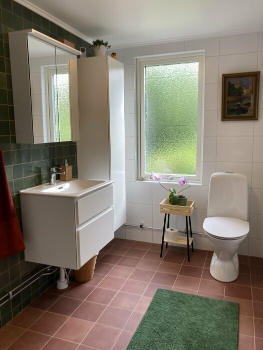 Ett rymligt och ljust badrum med gröna och vita kakel, toalett, handfat, spegelskåp och fönster.