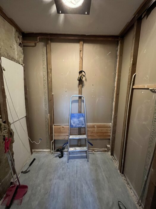 Ett pågående renoveringsrum med en stege, osynlig vägg och byggnadsredskap på golvet.