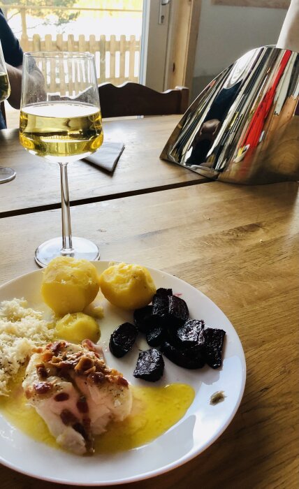 Måltid med potatis, kött, rödbetor, sås, ost, vin, träbord, inomhus och en speglande metallobjekt.