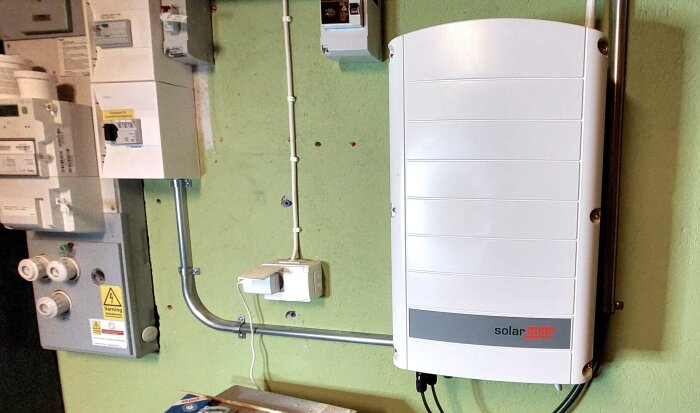 Solenergiomvandlare monterad på vägg bredvid elektriska säkerhetsbrytare och kablar.