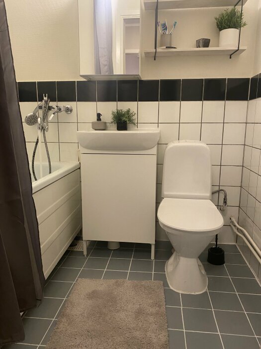 Ett rent, minimalistiskt badrum med vit och svart kakel, toalett, handfat, och duschdraperi.