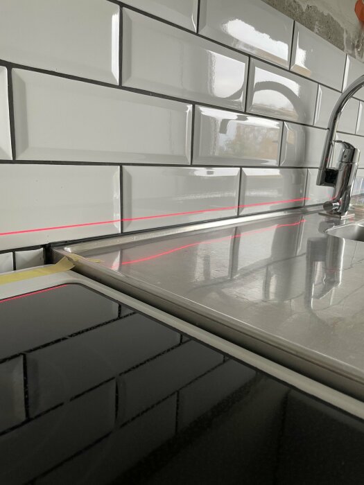 Kök med vita kakelväggar, bänkskiva, spishäll och röd laserlinje för mätning eller installation.