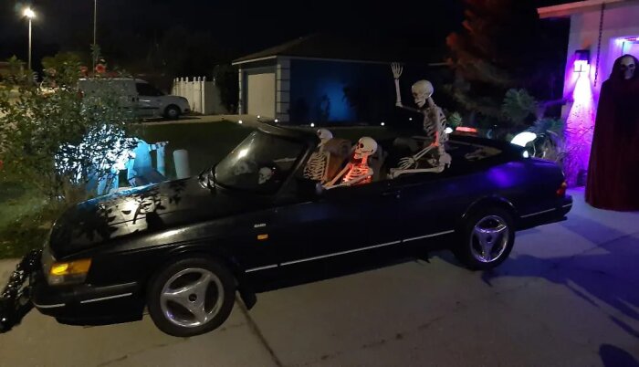 Cabriolet med skelett, kväll, Halloween-tema, skräckfigur, utomhus, mörk bakgrund, dekorativ belysning, firande.