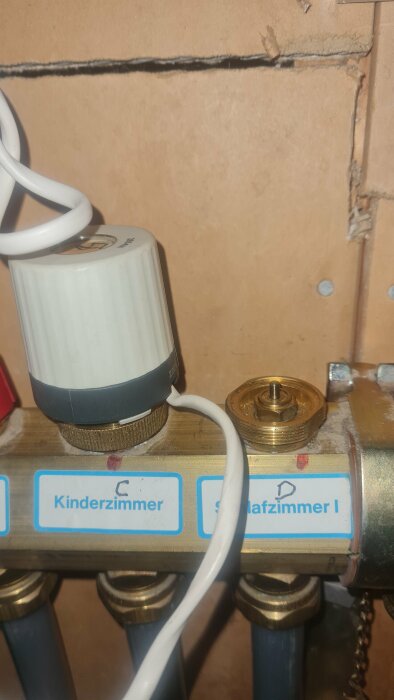 Värmeregulator på rörledning märkt "Kinderzimmer" och "Schlafzimmer I" mot brunt bakgrund.