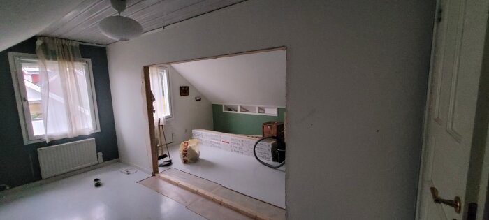 Tomt rum med pågående renovering, öppen vägg, isoleringsmaterial, byggdam och verktyg synliga.