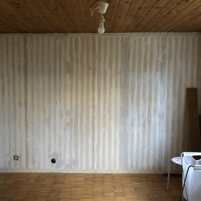 Ett tomt rum med trägolv, träpanel i taket, vägg under renovering.