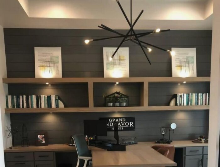 Modernt hemmakontor, inbyggd hylla, skrivbord, dator, bokhyllor, konstverk, industriell taklampa, stol, mörka nyanser.