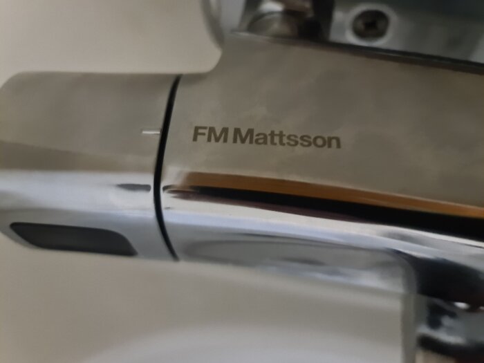 Närbild av kran, FM Mattsson logo, krom finish, badrumstillbehör, modern design, vattenkontrollutrustning.