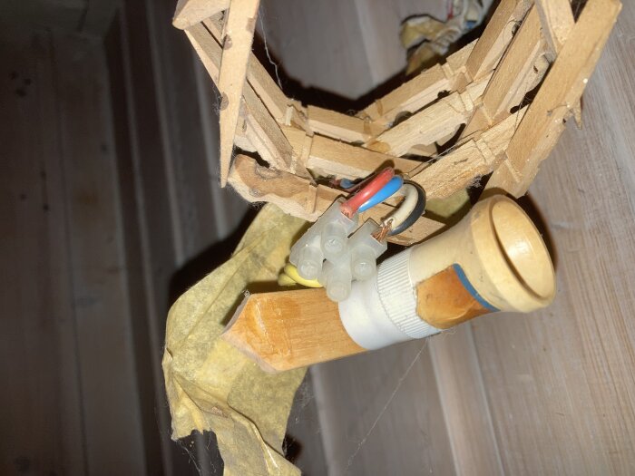 Öppen elektrisk koppling med tejpat rör och kabelskor inne i brutet tak. Farlig installation, behöver yrkesmässig reparation.