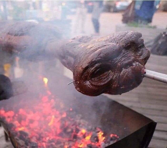 Ett grillat grisshuvud över öppen eld med suddig bakgrund.