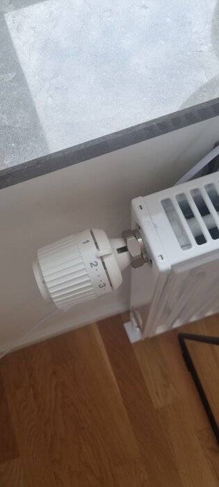 Termostat på radiator inställd på nivå tre, trägolv, del av fönster och stenbänk.