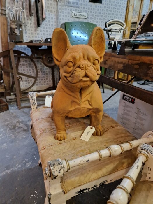 Terrakotta fransk bulldogg skulptur på slitet bord i en verkstadsinred miljö.