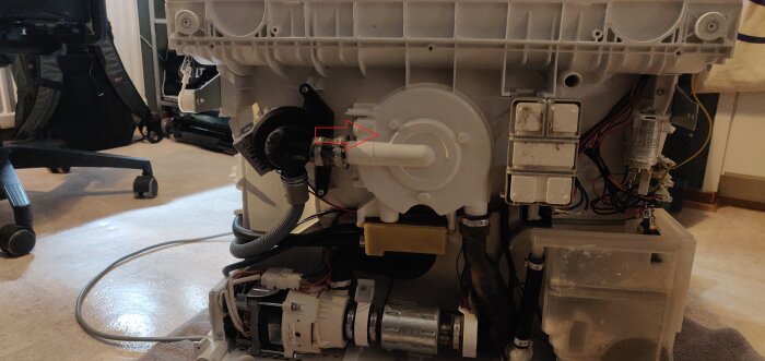 Tvättmaskin uppbruten, visar interna komponenter, motor, ledningar och mekaniska delar; indikerar reparation eller underhåll.