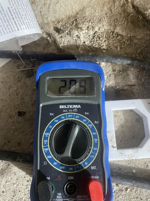 Multimeter visar 20.9, otydlig enhet, på en smutsig yta bredvid bruksanvisning.