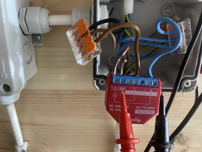 Elektrisk installation med kablar, dosa, grenklämma och hängande testenhet på en trävägg.