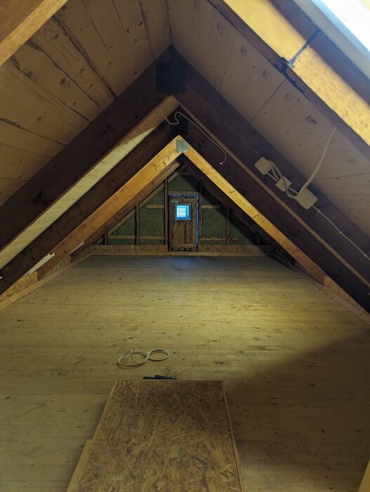 Vind med träbjälkar, isolering synlig, fönster, kabel på golvet, träplankor, ofärdigt utrymme.