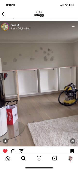 Ett rum med vita hyllor, en dammsugare, en matta, påbörjade reparationer eller sortering på väggen.