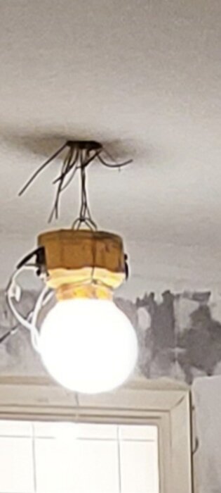 En lampa hänger från taket med synliga ledningar och skadad takyta ovanför skåpsluckor.