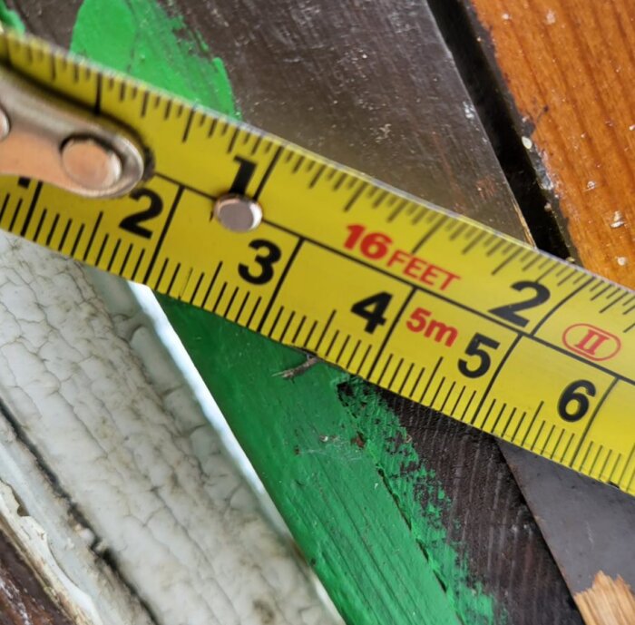 Måttband på träyta och grönt objekt. Mätning, verktyg, bygg, skala i tum och meter syns.