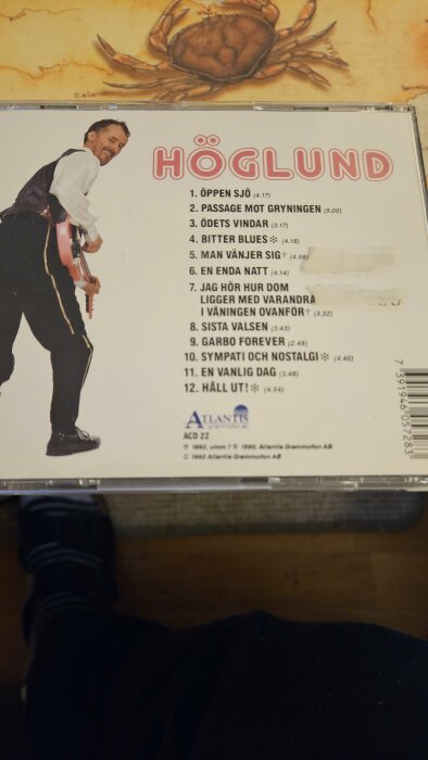 Ett CD-fodral med bild på artist och låtlista. Musikalbum, glad man med gitarr, skivomslag.