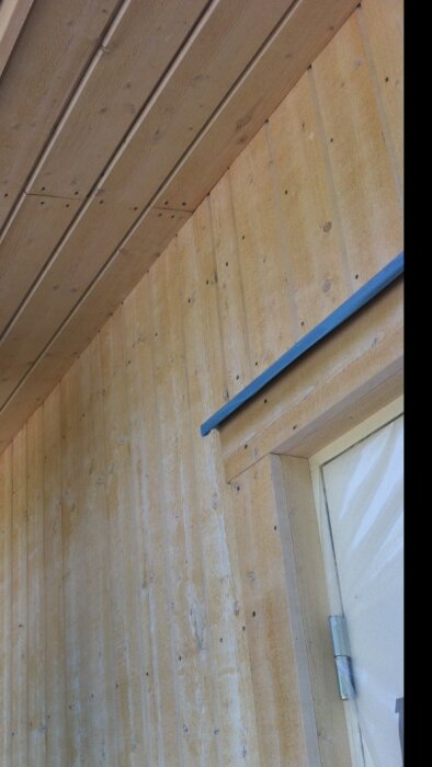 Träpanel vägg och tak, blå list, dörrkant synlig nertill.