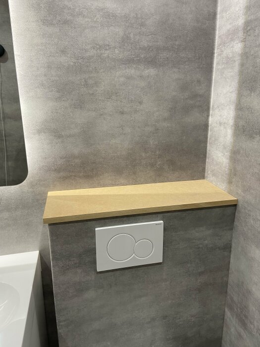 Modernt badrum, grå kakelvägg, inbyggd toalettspolningsknapp, trähylla, minimalistisk design.