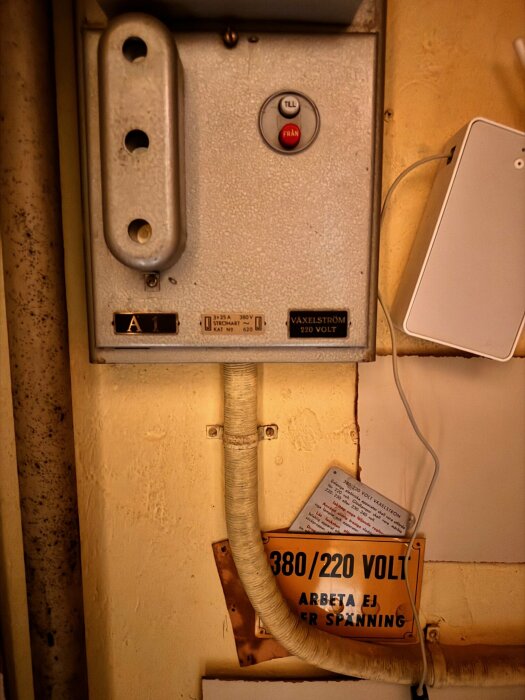 Gammalt elektriskt skåp med varningsskyltar, omkopplare och kablar på en smutsig vägg.