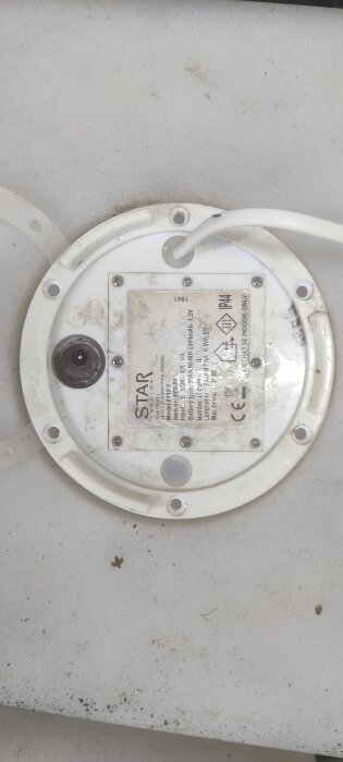 Ett smutsigt, vitt elektroniskt apparatskal med etiketter och kabel, troligen avsedd för inomhusbruk.